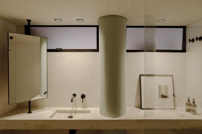 Bathroom vanity with stone countertop, circular column, wall-mounted taps, and horizontal clerestory windows