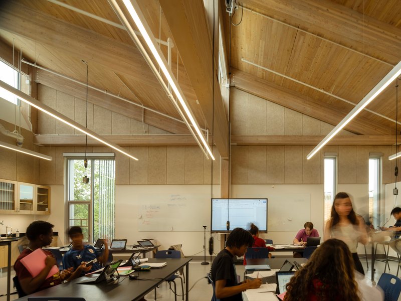 Classroom interior with vaulted timber ceiling, linear pendant lights, and occupants working at tables