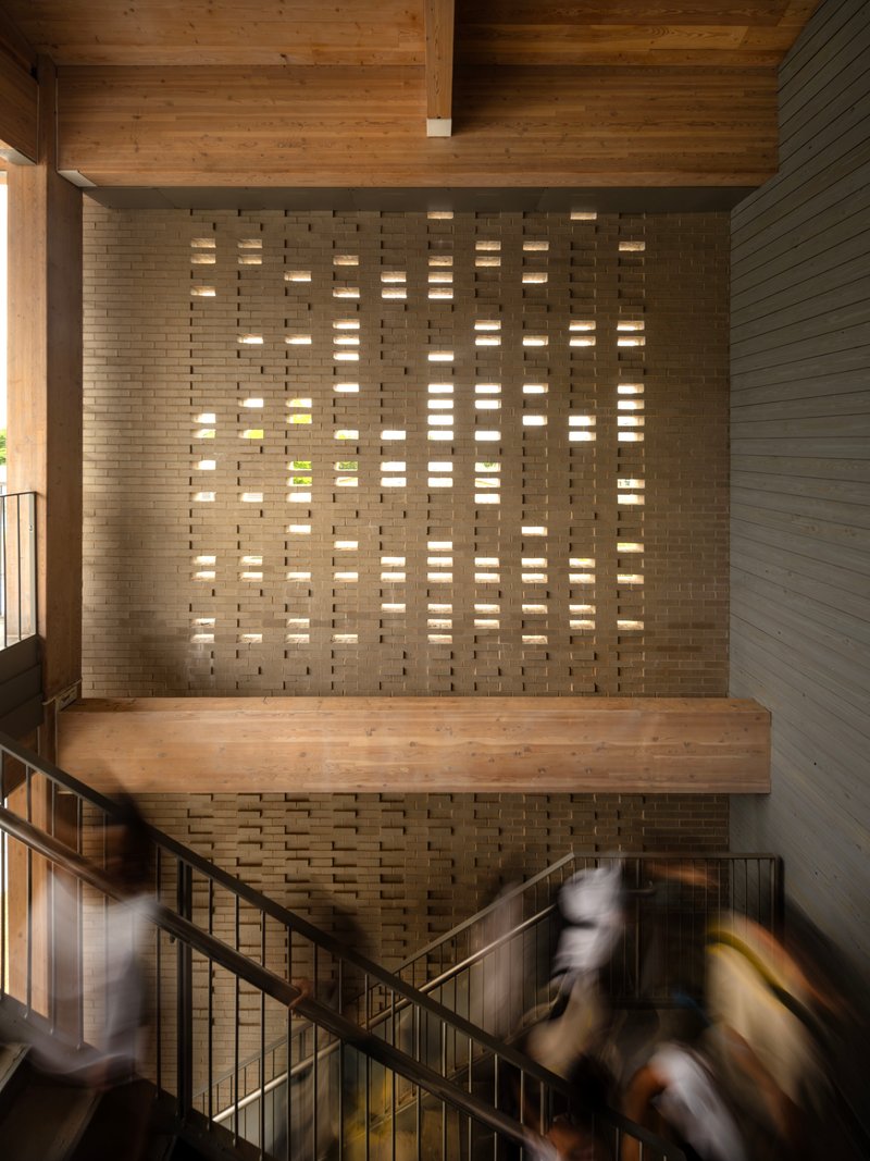 Perforated brick stair wall with light filtering through openings as people descend the steps
