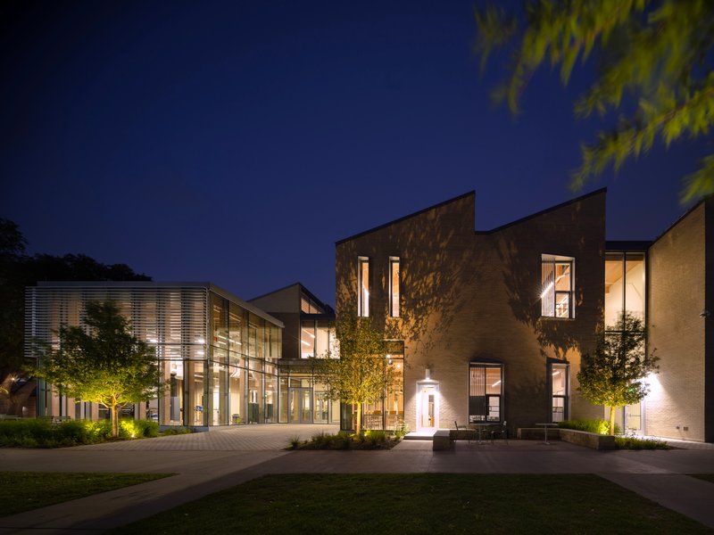 Illuminated complex at night showing the glass-walled wing and angular stone volumes across the plaza