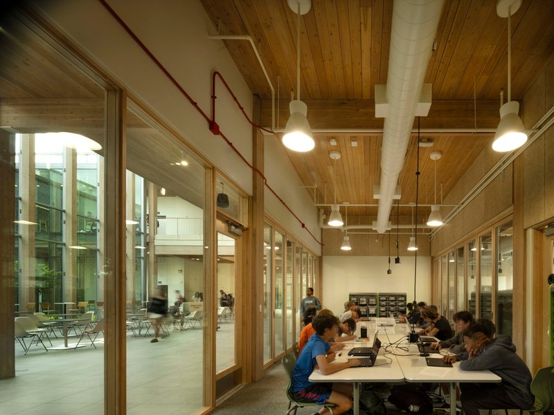 Study room with exposed timber ceiling, pendant lights and red conduit running along glass wall