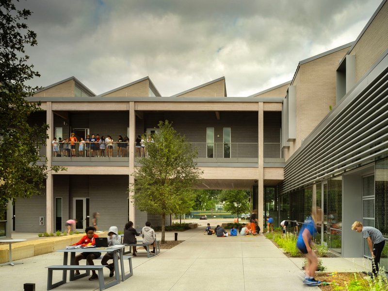 Covered outdoor courtyard with sawtooth roofline and students sitting at benches below colonnade