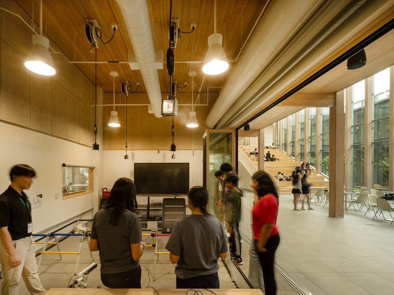 Glass-walled classroom space with timber ceiling and people gathered near a presentation screen