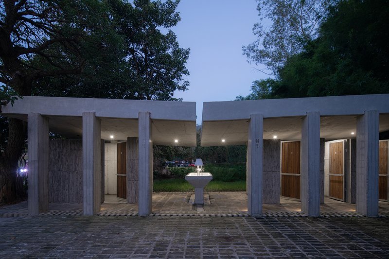 Covered colonnade at twilight with concrete columns framing doorways and a central fountain
