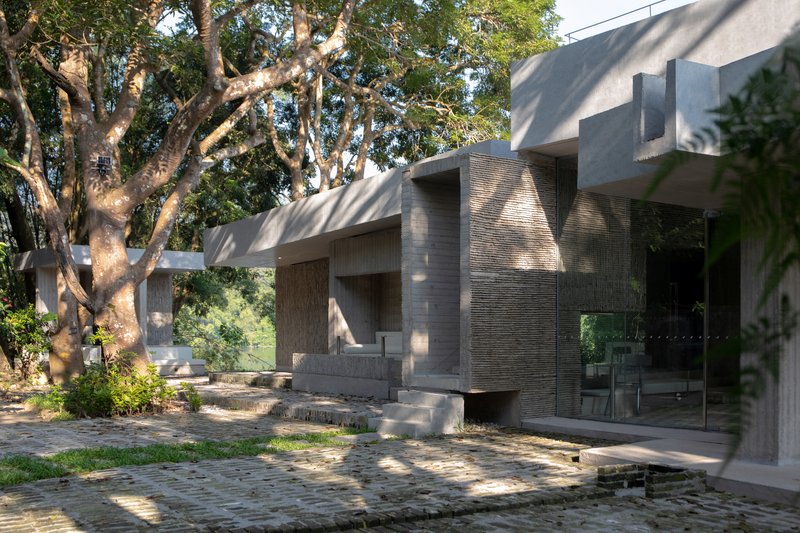 Courtyard with permeable paving, ribbed stone column and dappled morning light filtering through the trees