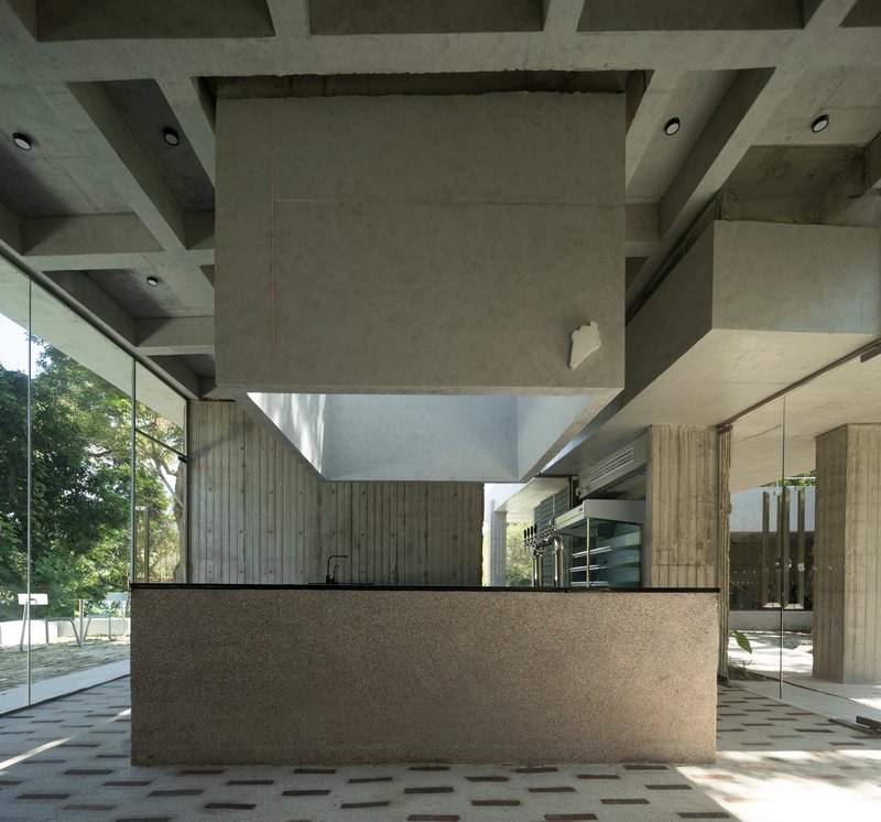 Interior reception counter with terrazzo base and vertical timber cladding beneath a coffered concrete ceiling