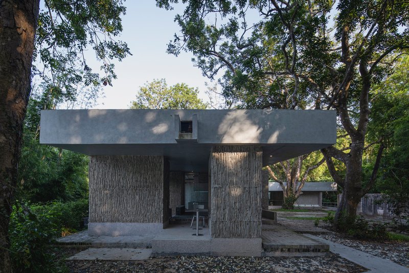 Elevated concrete pavilion with vertical timber cladding supported by cylindrical columns among mature trees