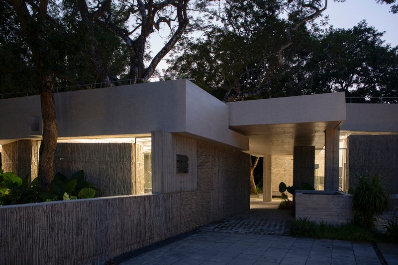 Entry courtyard with illuminated overhangs and vertical timber walls at dusk among tropical vegetation