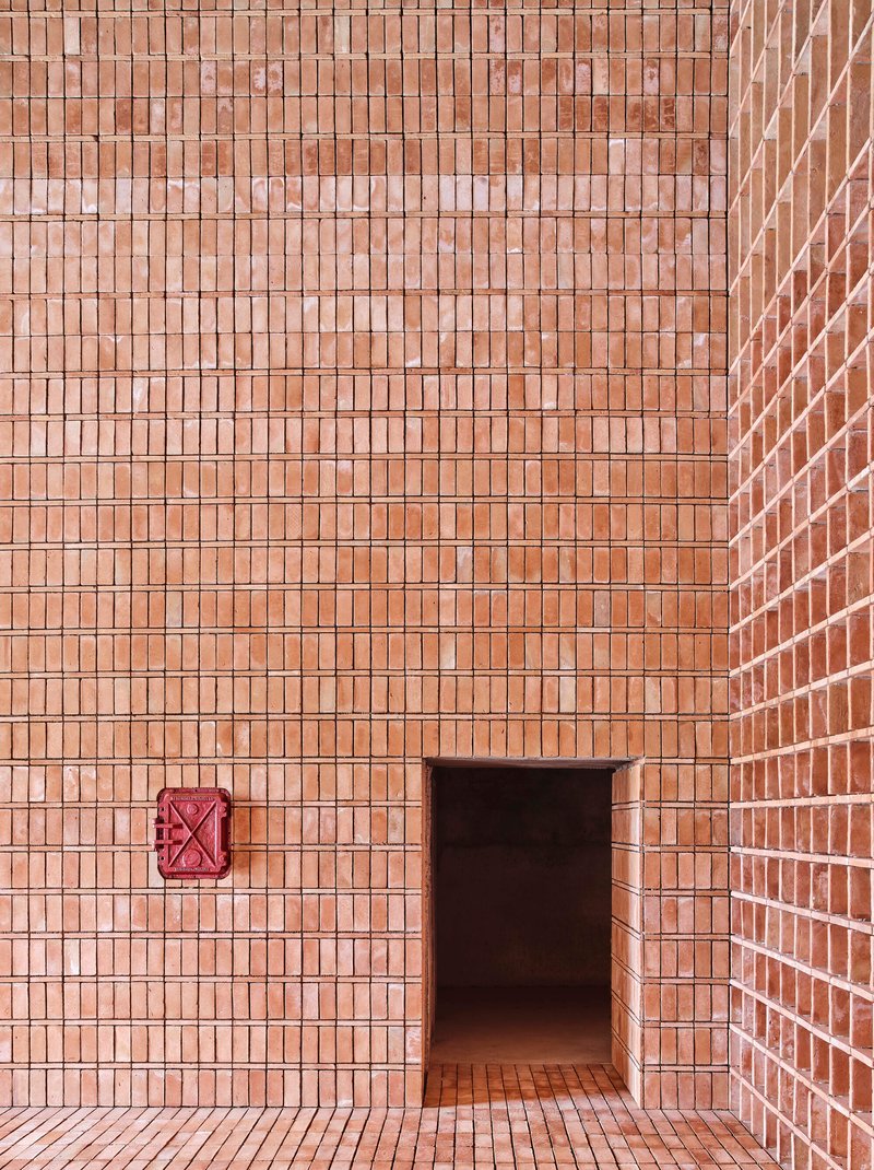Corner detail of brick wall with a recessed doorway and red metal ventilation grill