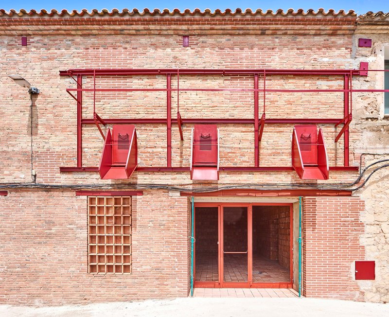 Street facade showing red metal awning structure above glazed entry doors and brick grid window