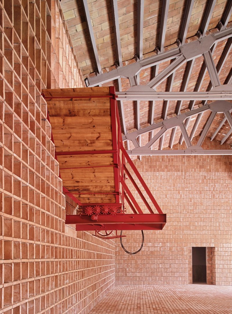 Red steel balcony with timber platform projecting from the perforated brick wall beneath painted steel trusses