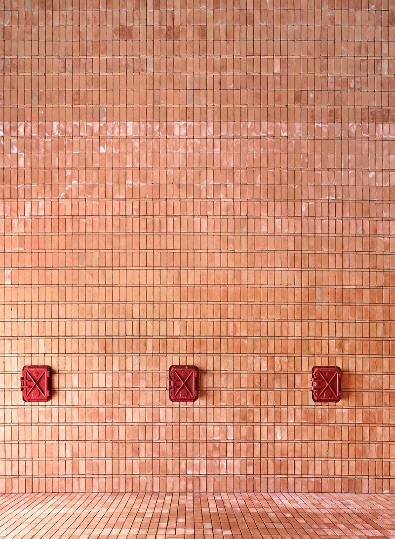 Exterior facade with terracotta mosaic tiles and three red decorative metal panels near the paved ground
