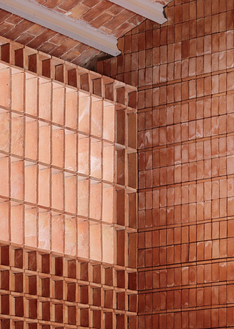 Close-up of terracotta brick corner showing alternating projecting courses and varied tile orientations under a timber ceiling