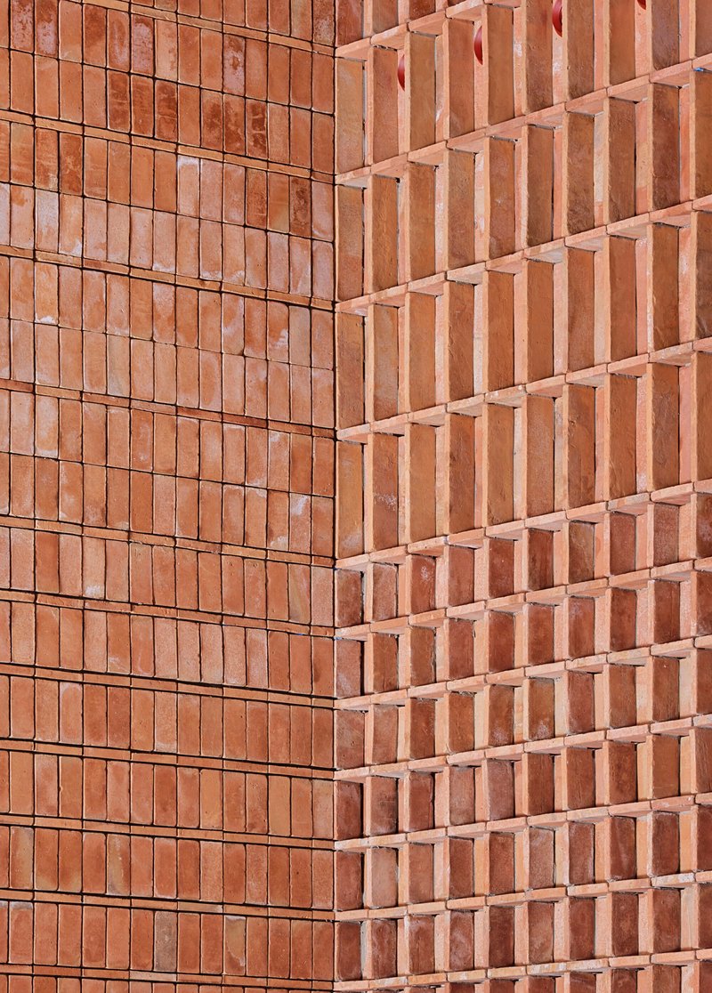 Corner detail of two terracotta brick facades meeting at differing textures and relief patterns