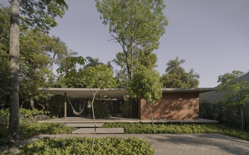 Street view of the single-story pavilion with floating concrete roof and timber-clad volume among trees