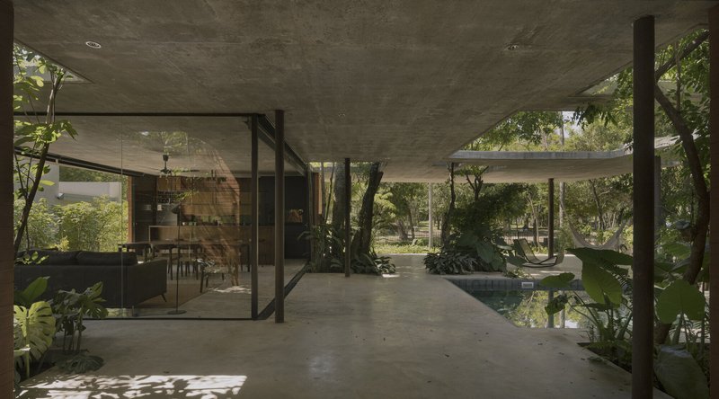 Open pavilion with concrete ceiling connecting glazed dining room to water garden and wooded landscape beyond