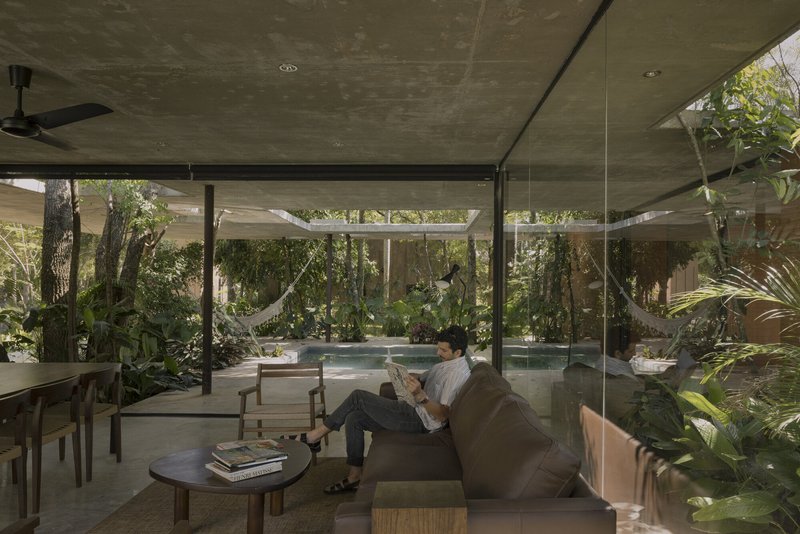 Interior living space with person reading on sofa overlooking pool and garden through floor-to-ceiling glass walls