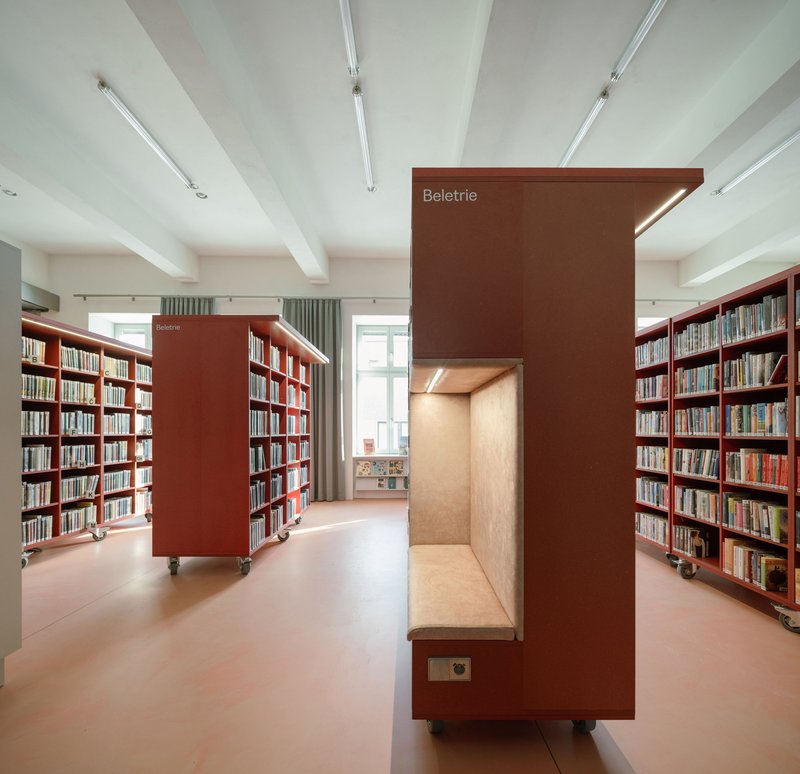 Freestanding coral booth with integrated bench seat flanked by mobile bookshelves on casters