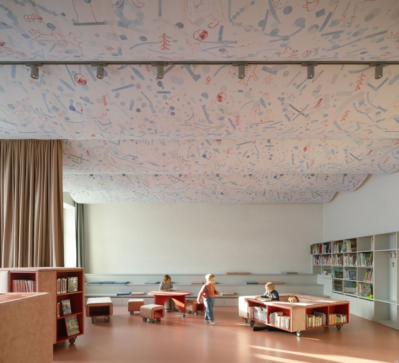 Library interior with illustrated fabric ceiling panels suspended over pink resin flooring with children playing