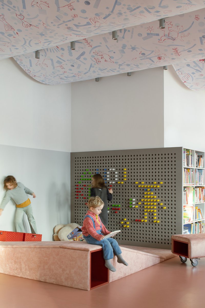 Pegboard wall with colored toys and children playing on stepped platform under draped illustrated ceiling