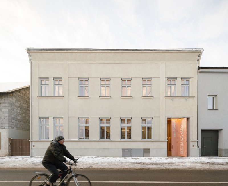 Street facade with pale plaster walls and symmetrical windows as a cyclist passes in winter
