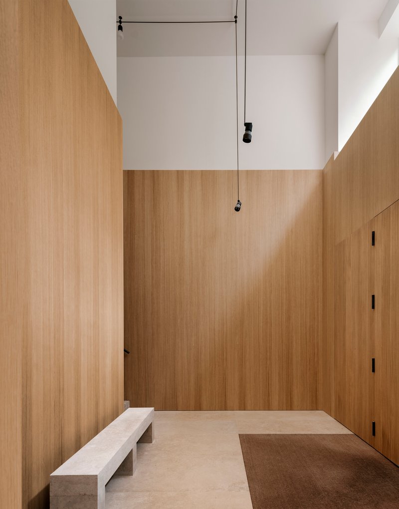 Double-height entrance hall clad in oak panels with pendant lights and stone bench seating