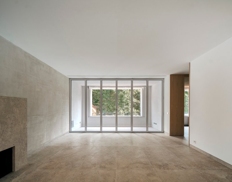 Empty room with large stone floor tiles and sliding glass doors overlooking a terrace with trees beyond