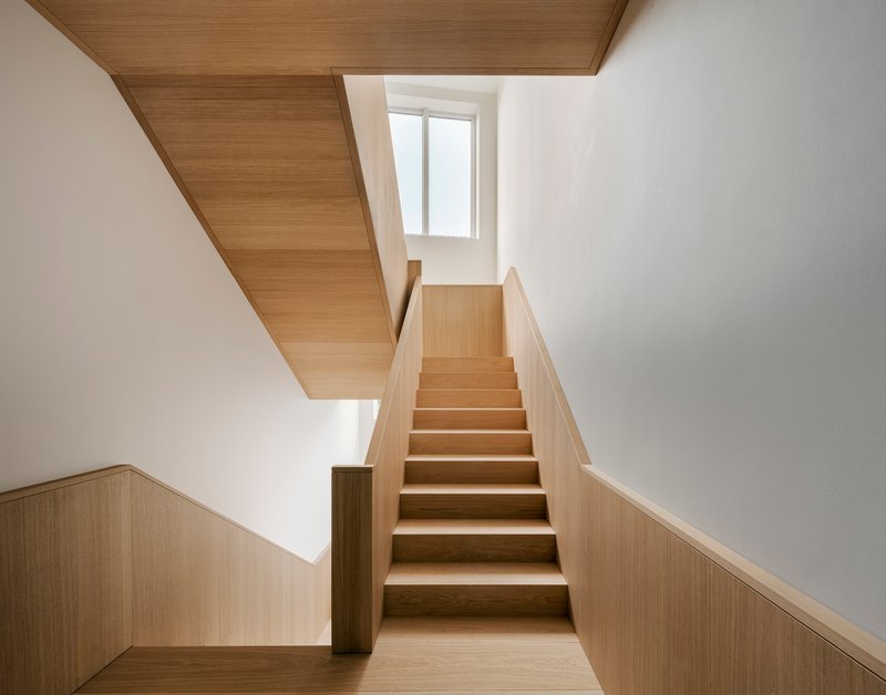 Timber staircase with wood-paneled ceiling and half-height wainscoting leading to a landing with a window