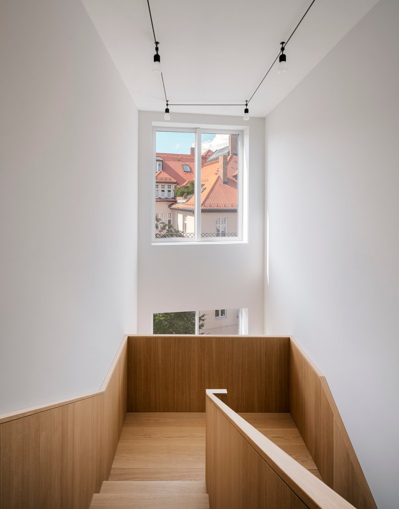 Double-height stairwell with timber balustrade and tall window framing clay-tiled rooftops outside