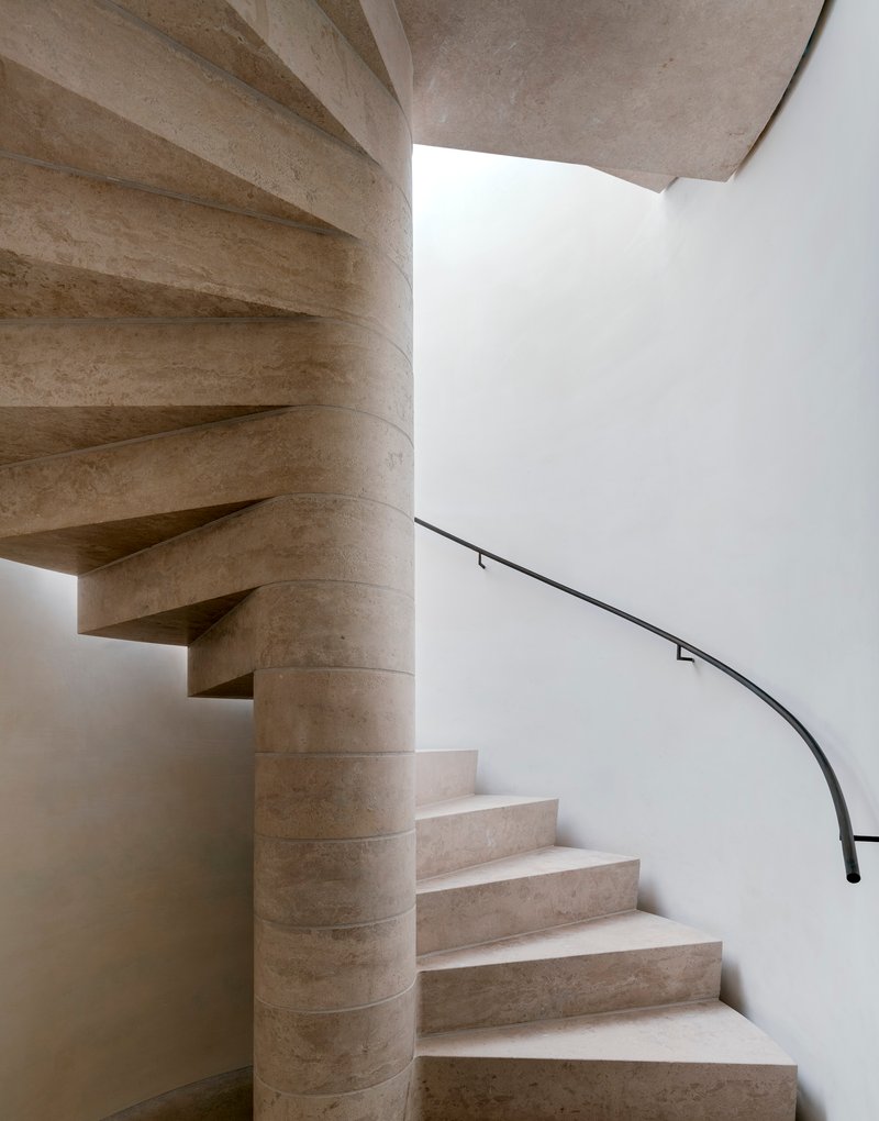 Curved stone staircase wrapping around a cylindrical core with a slender black metal handrail