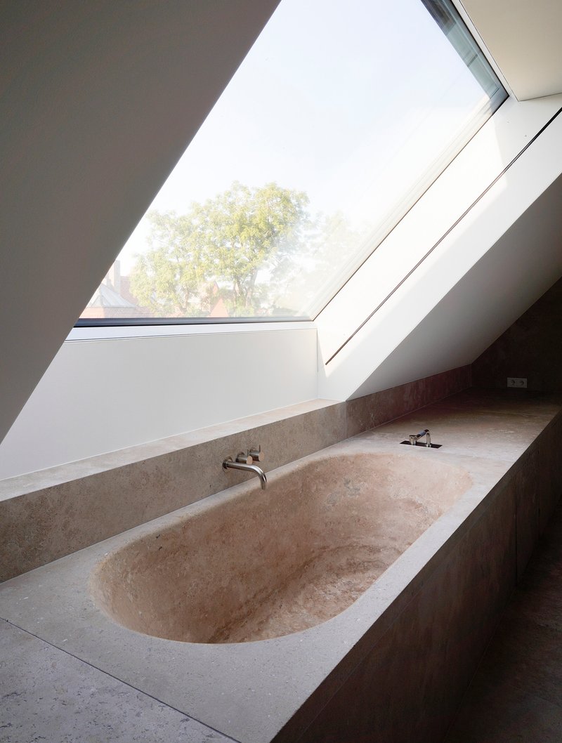 Travertine bathtub beneath an angled skylight with view to tree canopy outside