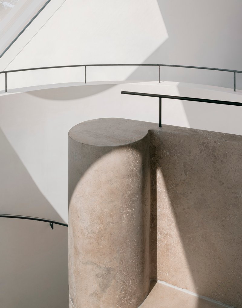 Curved stone column with cylindrical projection beside white spiral staircase with black railings