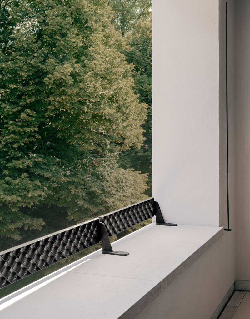 Detail of a recessed balcony with patterned metal railing and white frame overlooking green foliage