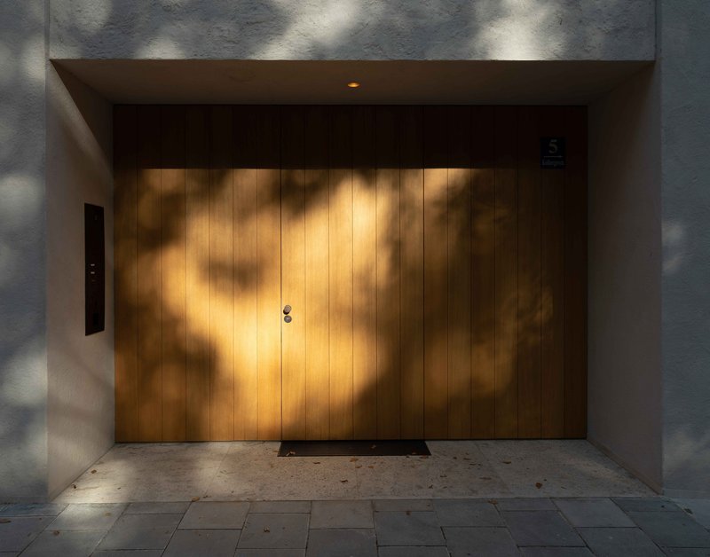 Recessed entrance with vertical timber door panels dappled by leaf shadows in afternoon sun