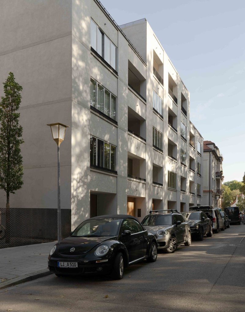 Four-story residential facade with recessed balconies and horizontal window bands along a parked street