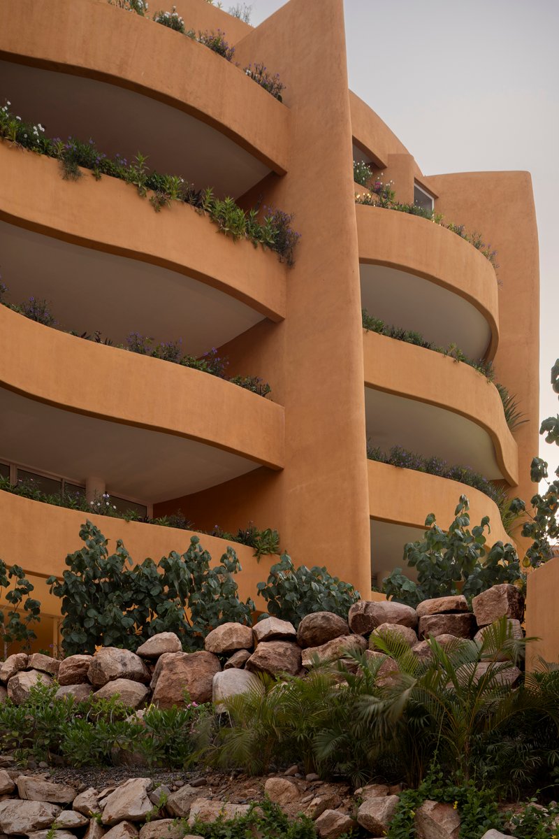 Curved balconies with planted edges rise above a terraced rock garden with cacti and ferns