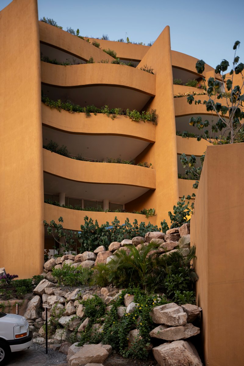 Planted balconies cascade down the ochre facade framed by a boulder retaining wall