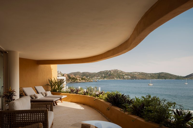 Curved terrace with lounge chairs and planted bed overlooking the bay and hillside beyond