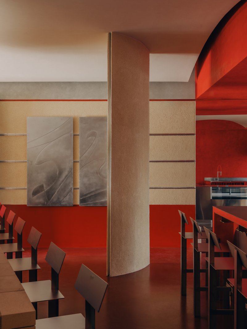 Dining area with cylindrical column, horizontal wall bands, and red resin flooring under warm light