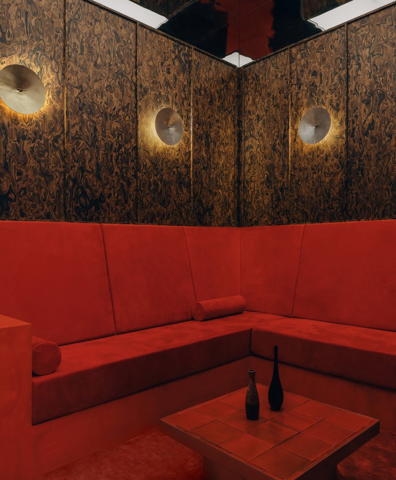 Corner banquette with red upholstery beneath decorative wood veneer walls and three disc sconces