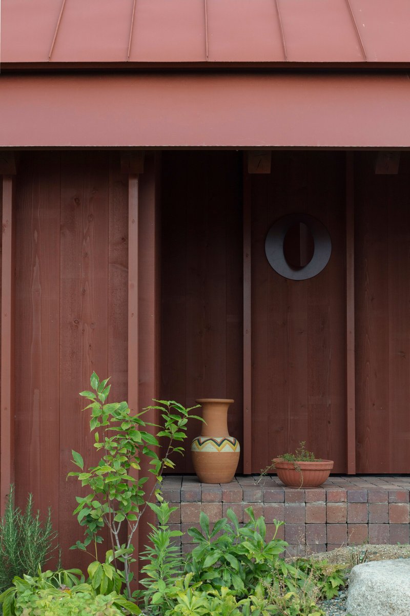 Timber slatted facade beneath a pink metal roof with potted plants on a tiled threshold