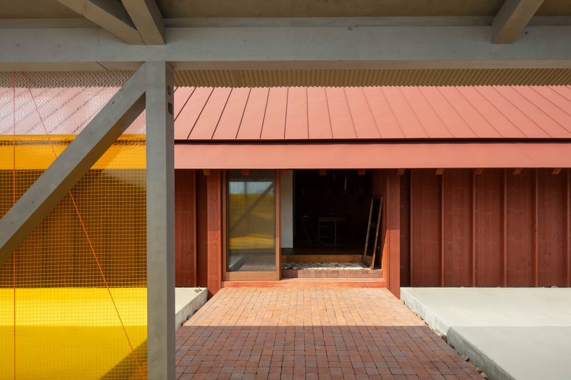 Covered porch with exposed timber beams, red metal panel walls and yellow wire mesh courtyard beyond