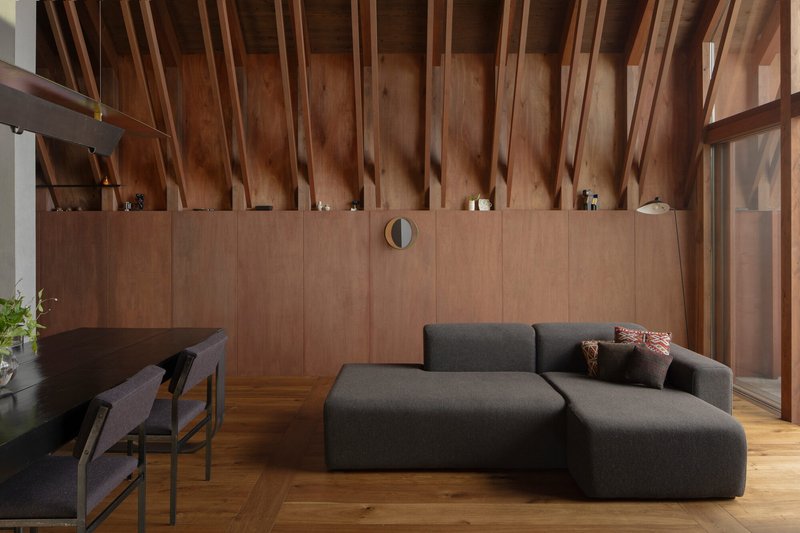 Living area with wood paneling, exposed timber structure and grey upholstered seating facing planted terrace