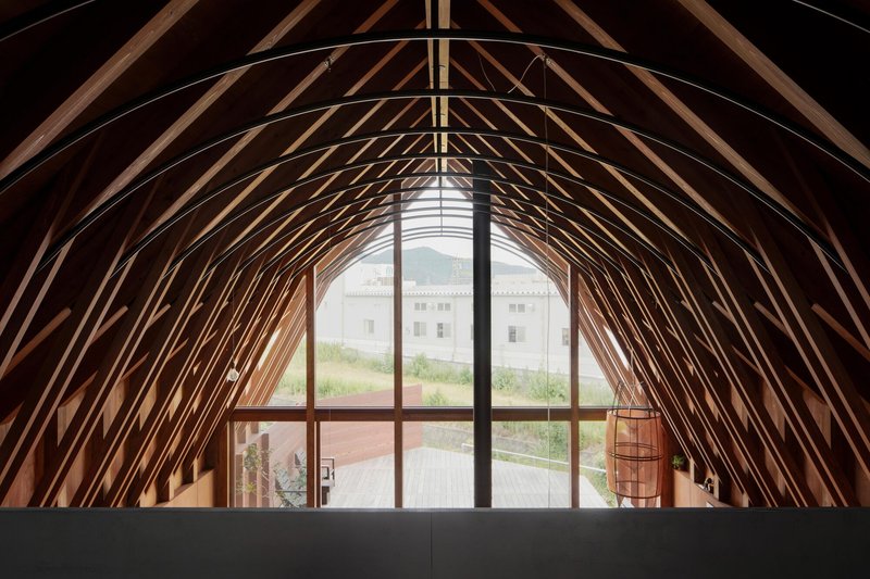 Arched timber rib ceiling framing tall glazed opening with view to courtyard and neighboring structure