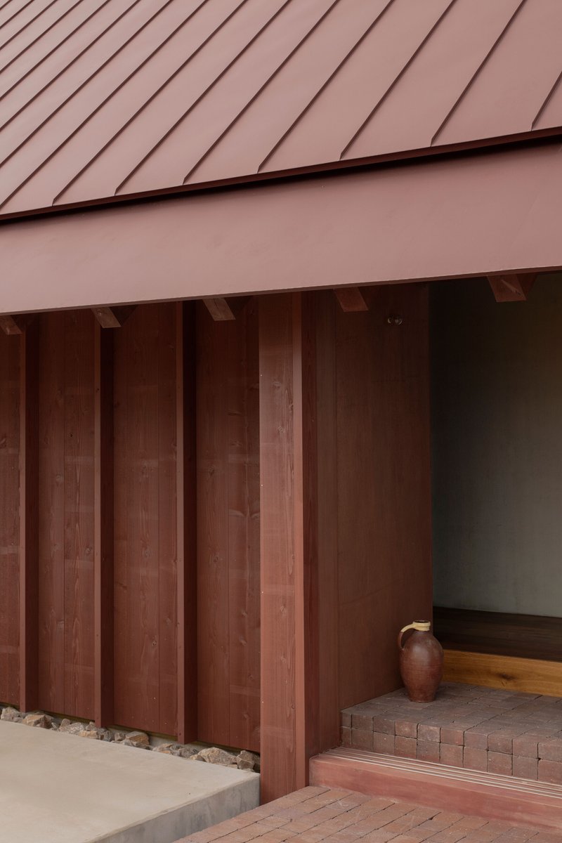 Entrance threshold with vertical timber cladding under a pink standing seam metal roof and tiled step