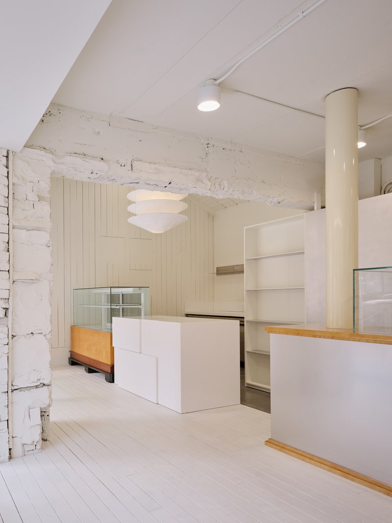 Stepped white display volume in front of an exposed white-painted stone wall