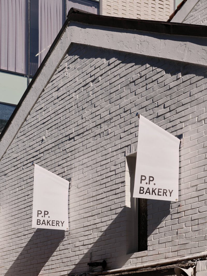 Two cloth banners reading P.P. BAKERY hung against a grey-painted brick gable