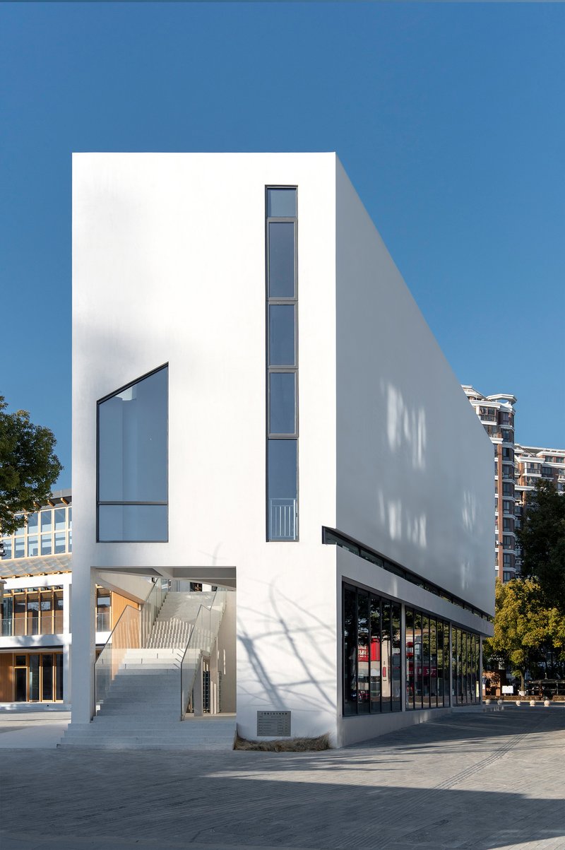 White rendered facade with vertical window slot and angled shadow in clear daylight