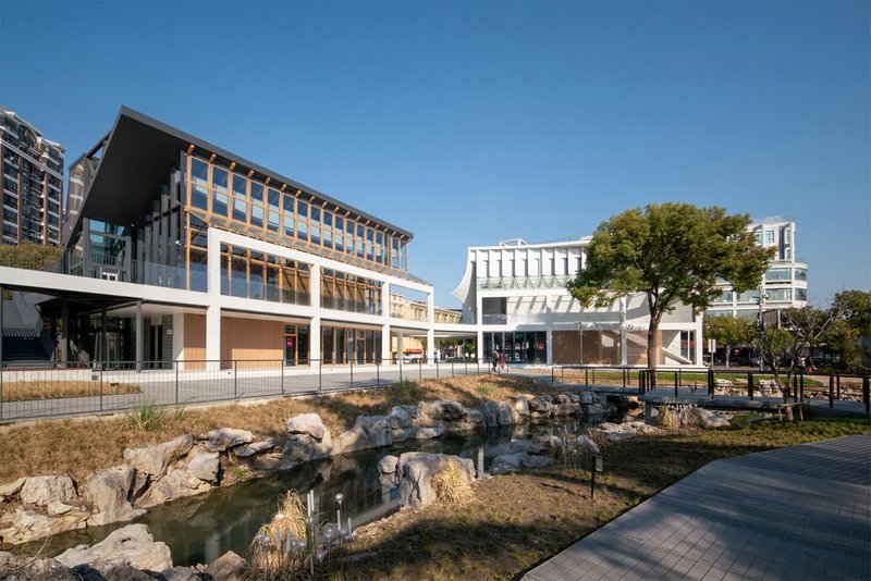 Multi-level building with timber and glass facades overlooking a rocky pond with dry grasses