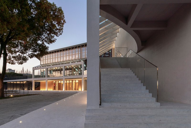 Exterior stone staircase with glass railing beneath a concrete overhang at dusk